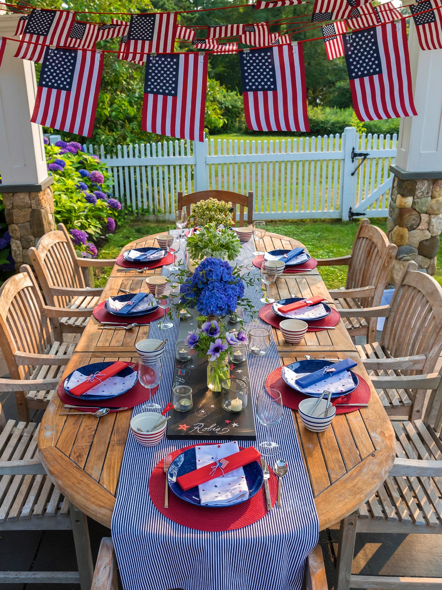 Outdoor Fourth of July table setting with flags, blue hydrangea centerpiece, and red white blue dinnerware