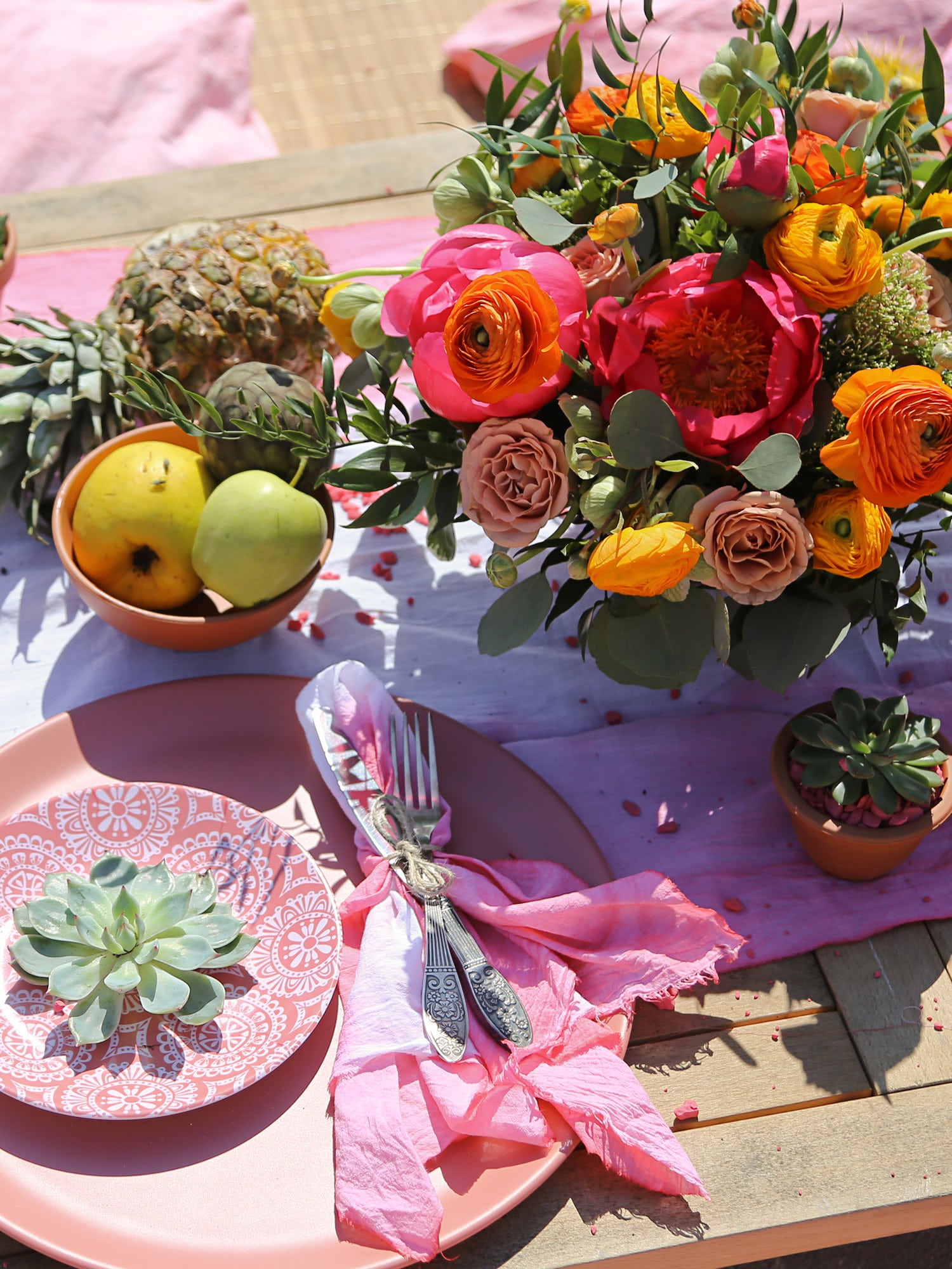 Summer table setting with pink and orange bouquet, fruit, succulents, and pink plates on a wooden table